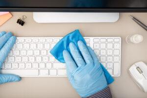 Hand mit Schutzhandschuh bei der Reinigung einer Tastatur mit Desinfektionsmittel