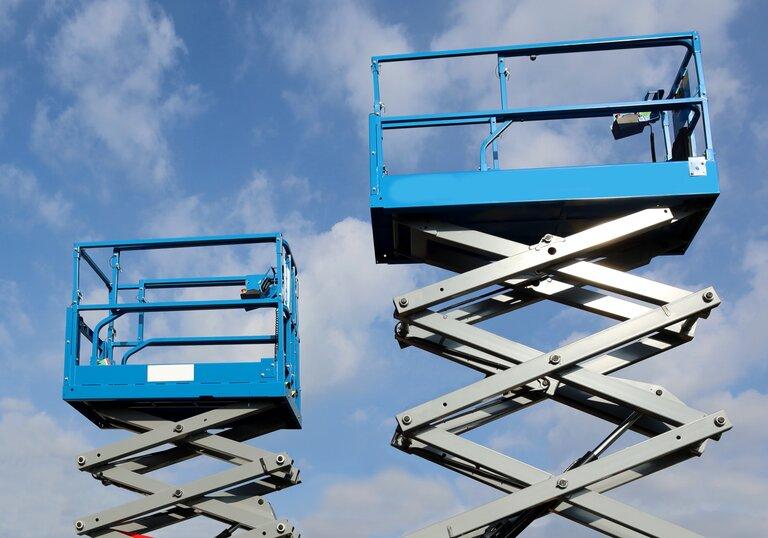 Zwei Arbeitsbühnen, genannt Scherenaufzug, ausgefahren vor blauem Himmel Hintergrund