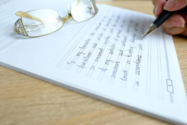Nahaufnahme weibliche Hand schreibt mit einem Stift auf Papier die Worte des Testaments, das Konzept einer rechtlichen Verfügung über ihr bewegliches und unbewegliches Vermögen im Falle des Todes einer Person für die Erben
