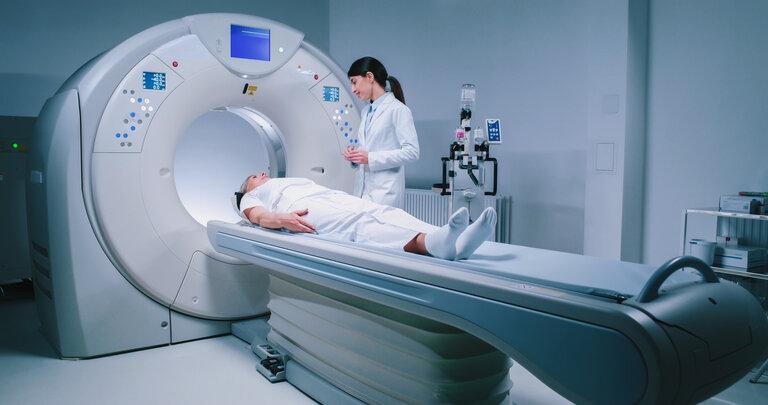 Medizinische Mitarbeiterin in Kittel vor MRT-Untersuchung. Ärztin bereitet Patient für Magnetresonanzverfahren vor. Der Patient liegt am CT-Scanner und wartet auf die Untersuchung.