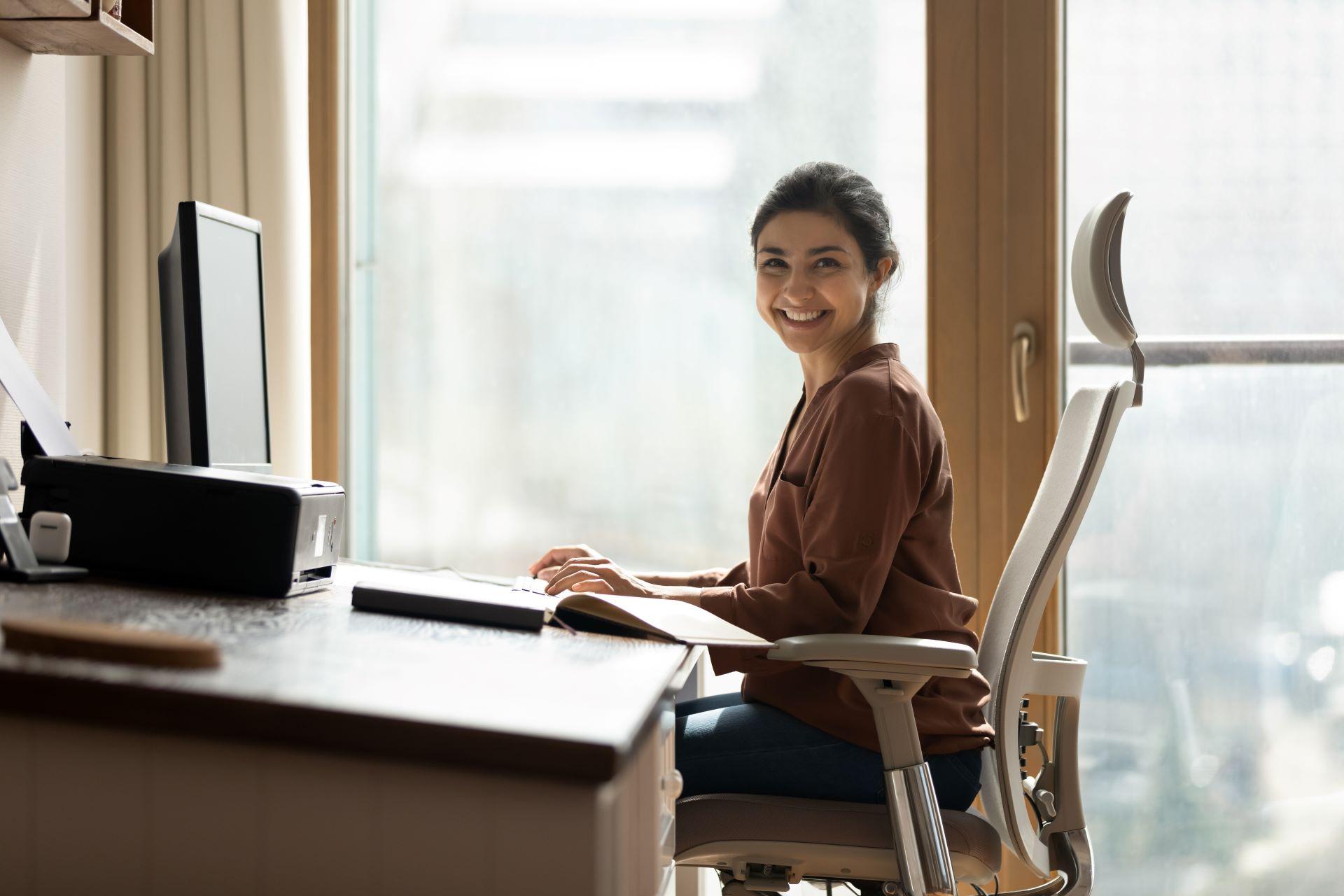 Frau sitzt an einem Schreibtisch in einem produktiven Home-Office, das durch natürlichen Lichteinfall und eine Zimmertür weiß unterstützt wird.