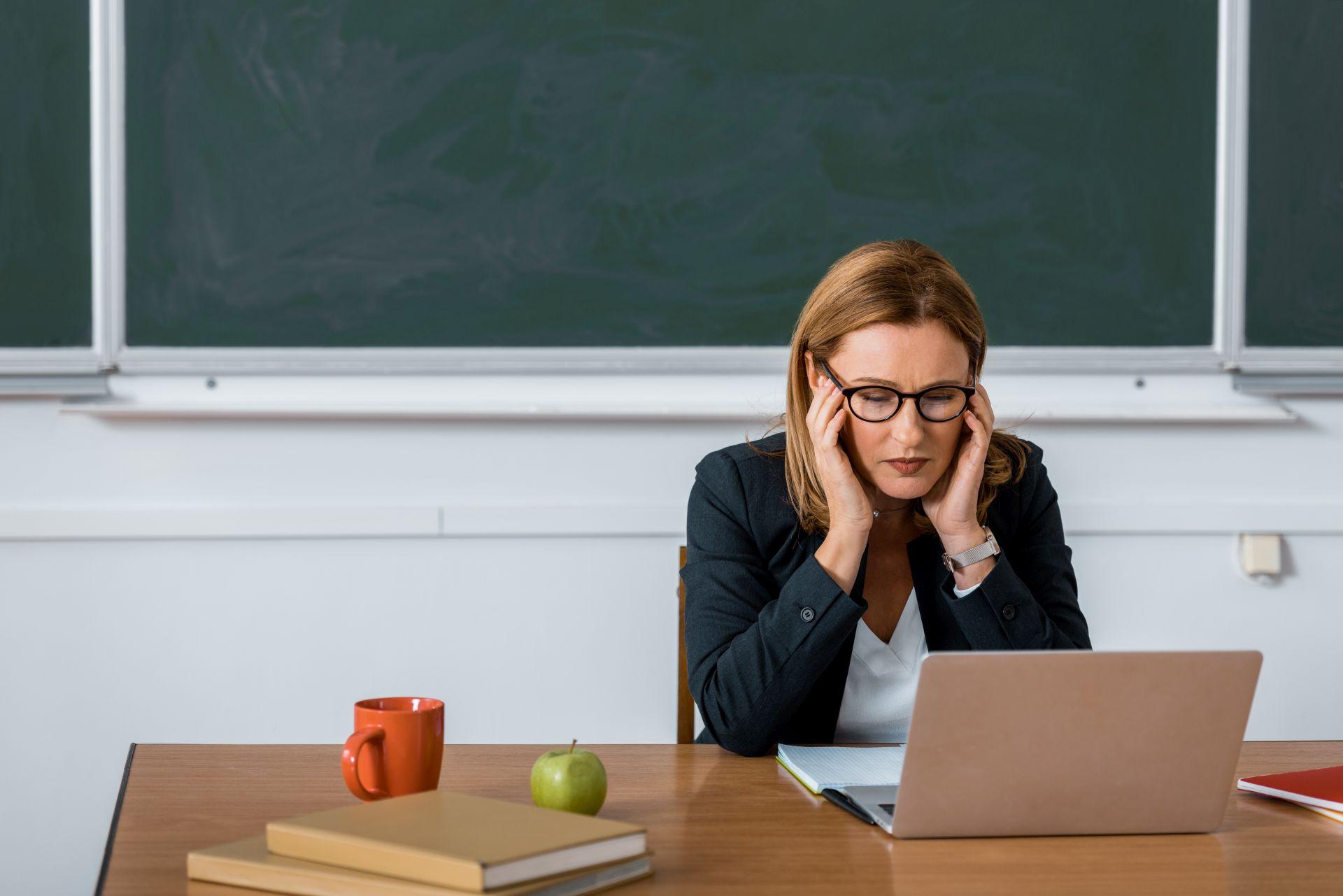 Gestresste Lehrerin am Schreibtisch, überlastet durch den Schulalltag – Absicherung durch eine Dienstunfähigkeitsversicherung