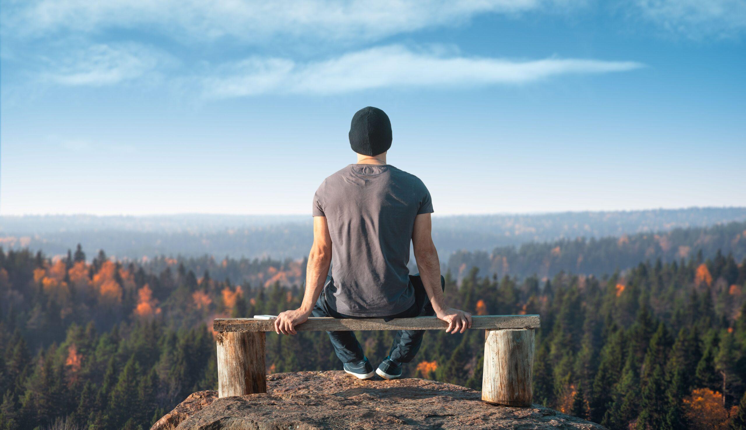 Ein Mann sitzt auf einer Bank in der Natur.