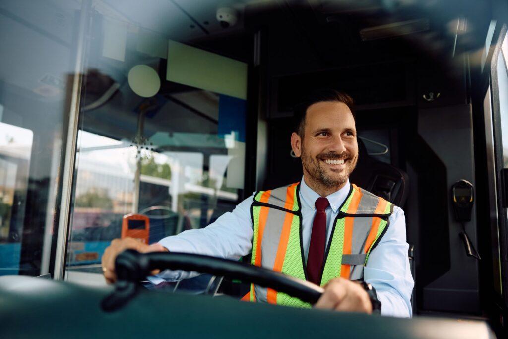 Freundlicher Busfahrer mit Warnweste am Steuer eines Busses.