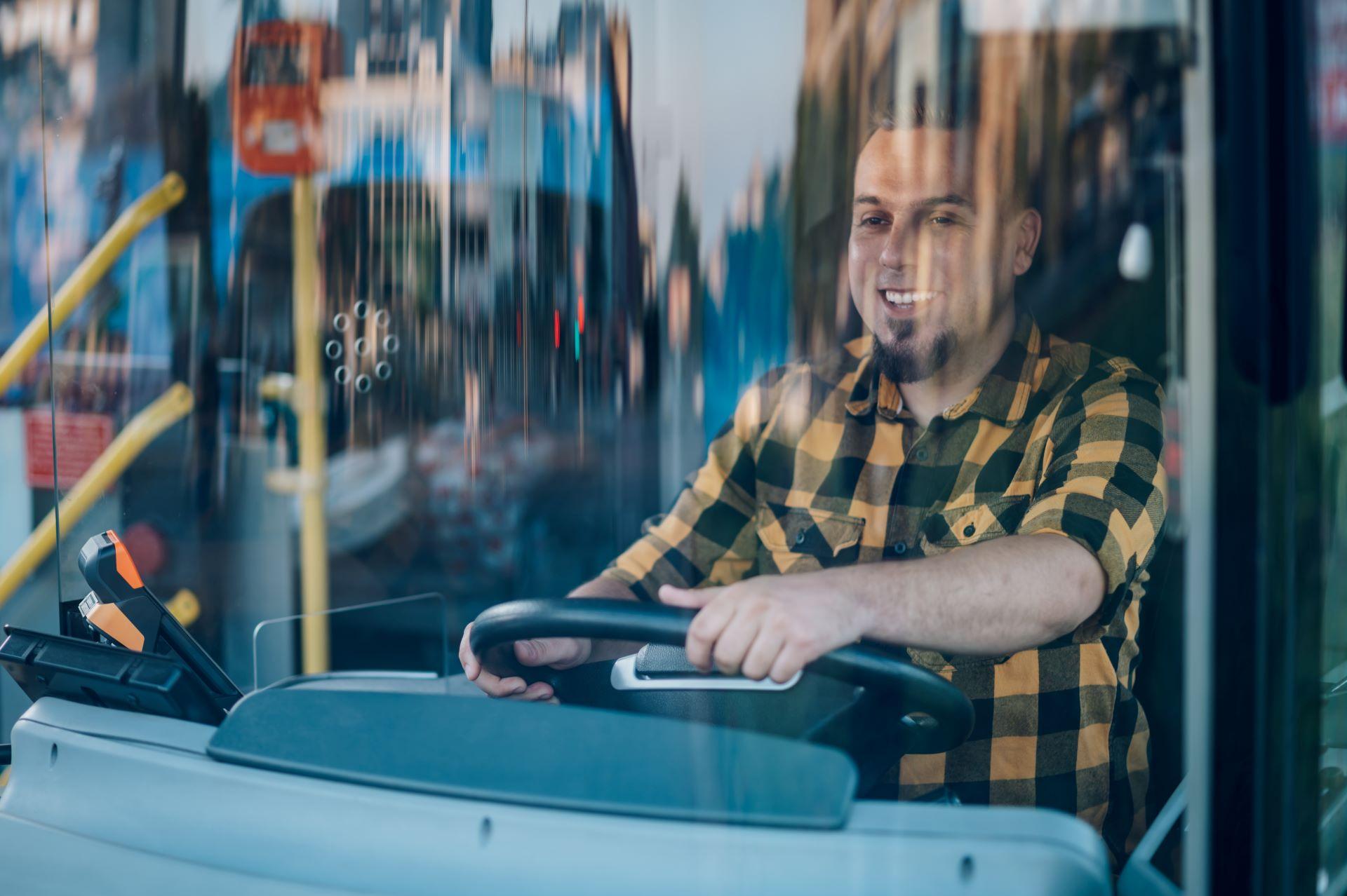 Busfahrer im gelben Hemd lenkt einen Bus im ÖPNV.