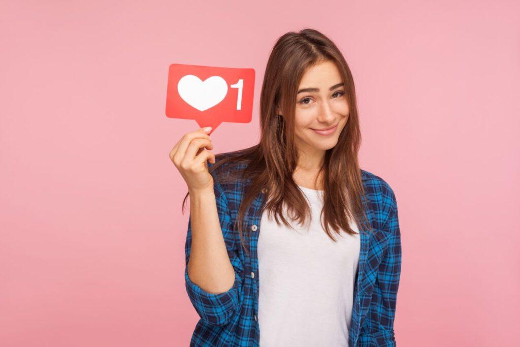 Frau hält ein Like-Symbol auf rosa Hintergrund – Symbol für Engagement und Kreativität einer Social Media Agentur.