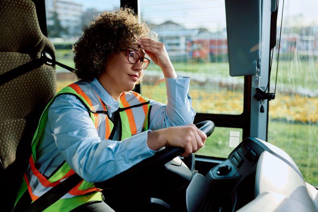 Busfahrerin mit Warnweste stützt den Kopf mit der Hand, wirkt erschöpft. Symbolbild für Stress im Berufsalltag und die Relevanz von CZV-Kursen für Entlastung und Stressmanagement