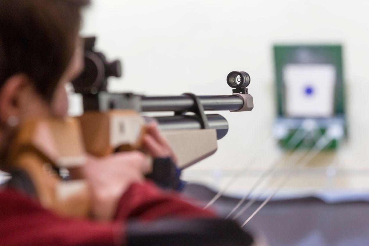 Person zielt mit einem Luftdruckgewehr auf eine Zielscheibe, Fokus auf Präzision und Technik im Schießsport mit CO2 Kapseln