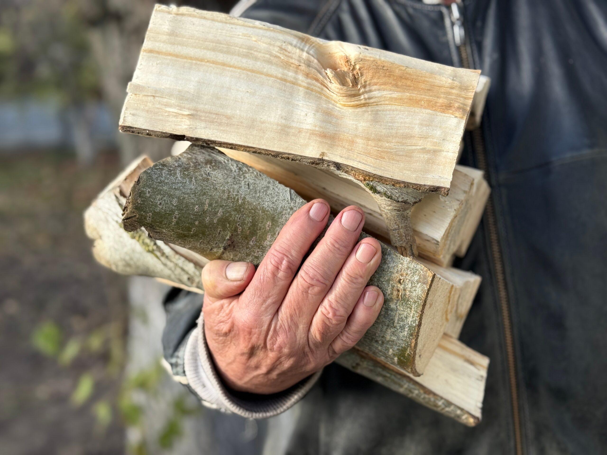 Hand traegt gespaltenes Kaminholz aus dem Holzlager im Freien