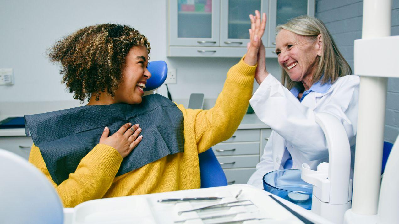 Glückliche Patientin in Essener Zahnarztpraxis gibt behandelnder Zahnärztin ein High Five nach erfolgreicher implantologie essen