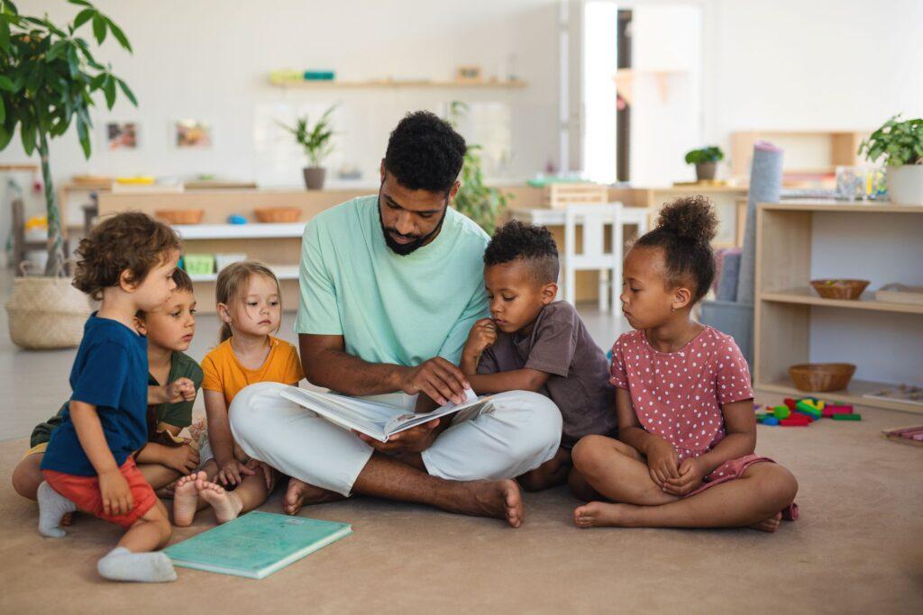 Erzieher liest mehreren Kindern im Kreis eine Geschichte vor im Kindergarten Schwabing
