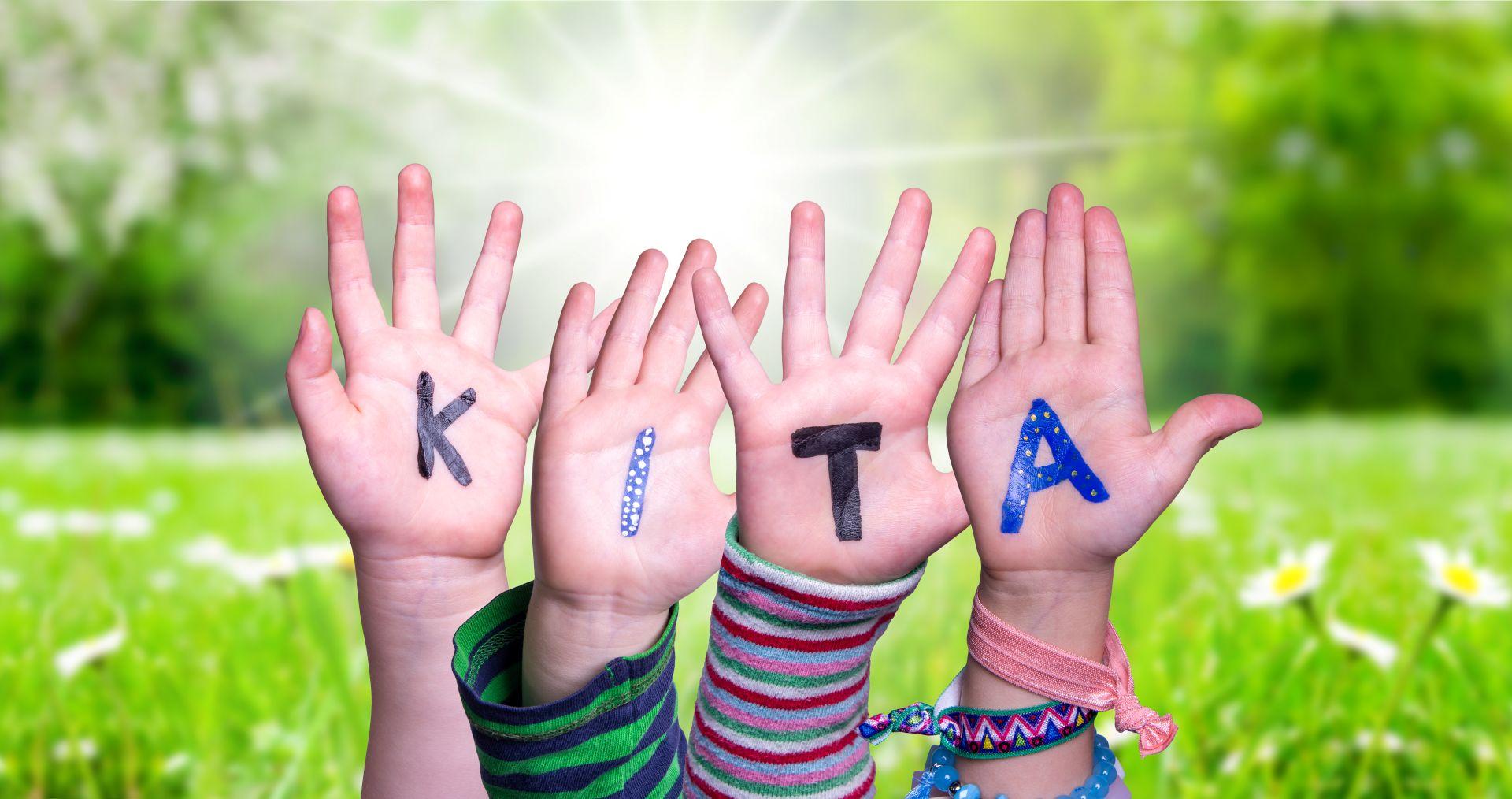 Kinder zeigen den Schriftzug KITA auf ihren Handinnenflaechen im Garten im Kindergarten Schwabing
