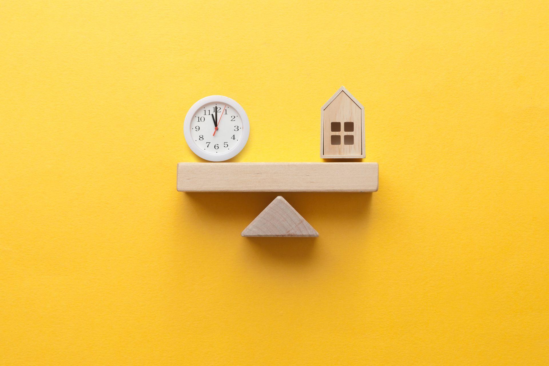 Holzhaus und Uhr im Gleichgewicht auf gelbem Hintergrund symbolisieren Balance zwischen Beruf und Familie im Kindergarten Schwabing