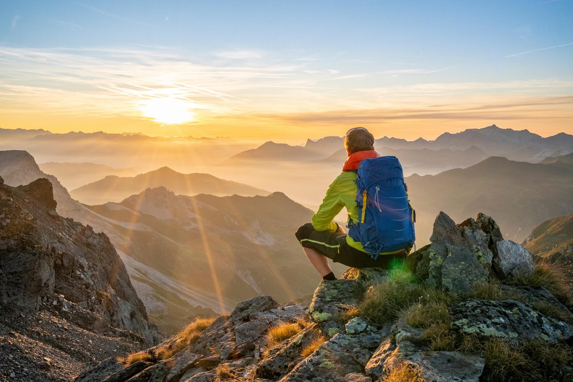 Wanderer sitzt auf Bergspitze mit Sonnenaufgang | Berghütte Österreich